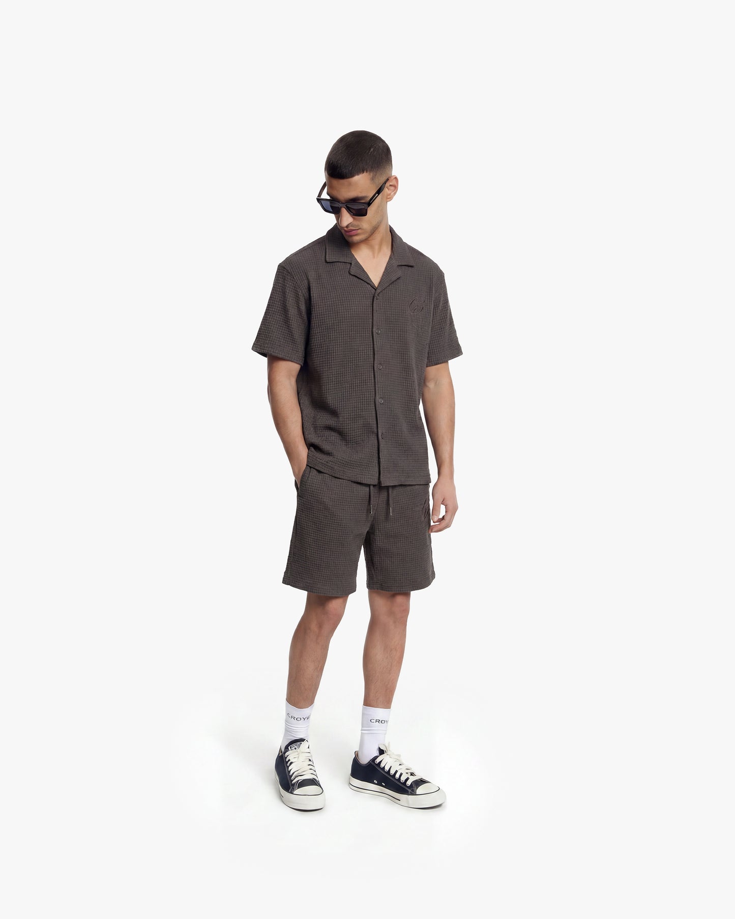 Man wearing a washed brown waffle shirt and matching shorts, black sunglasses, and sneakers.