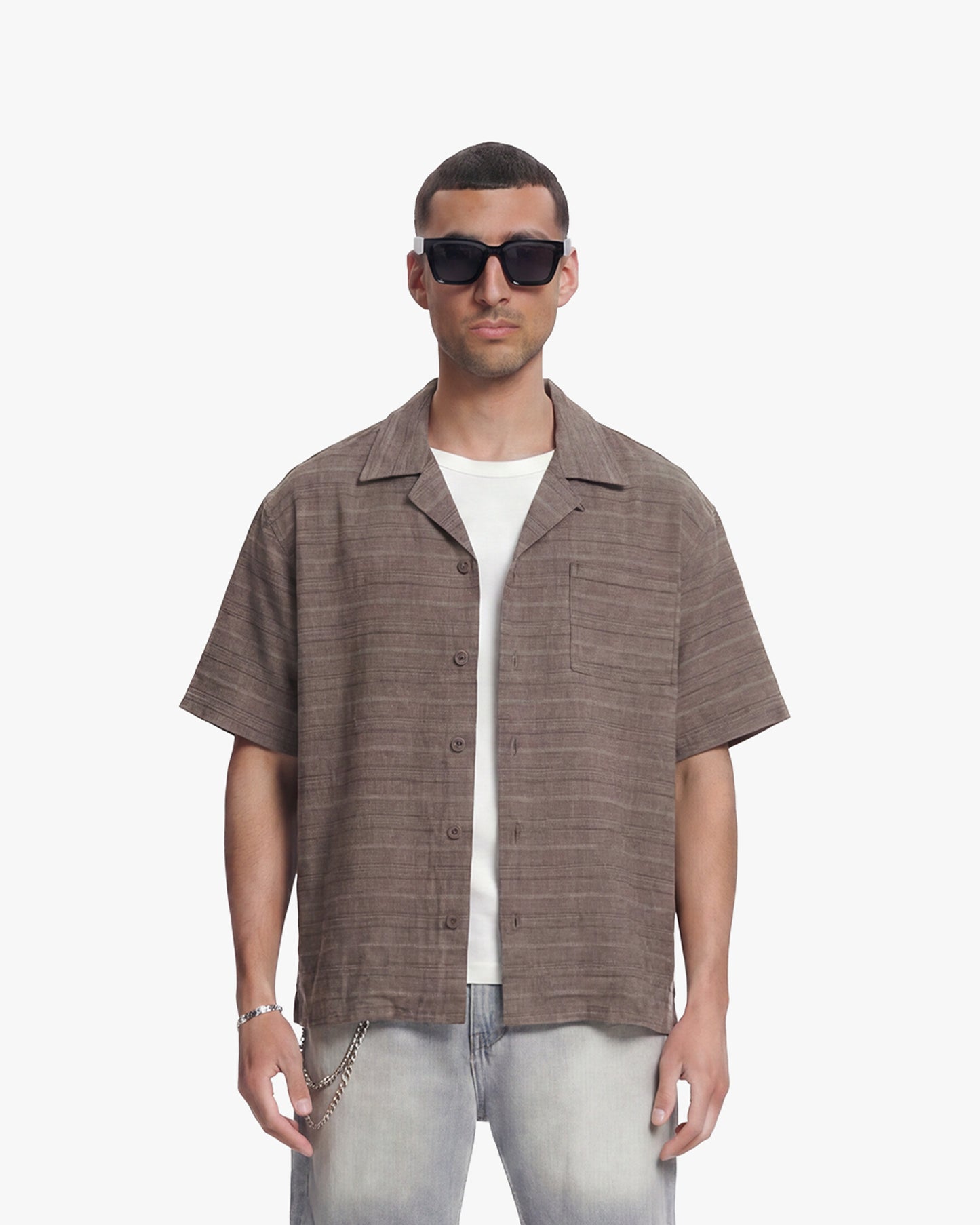 Man in vintage brown flannel shirt, short-sleeved with chest pocket, over a white tee and light wash jeans.