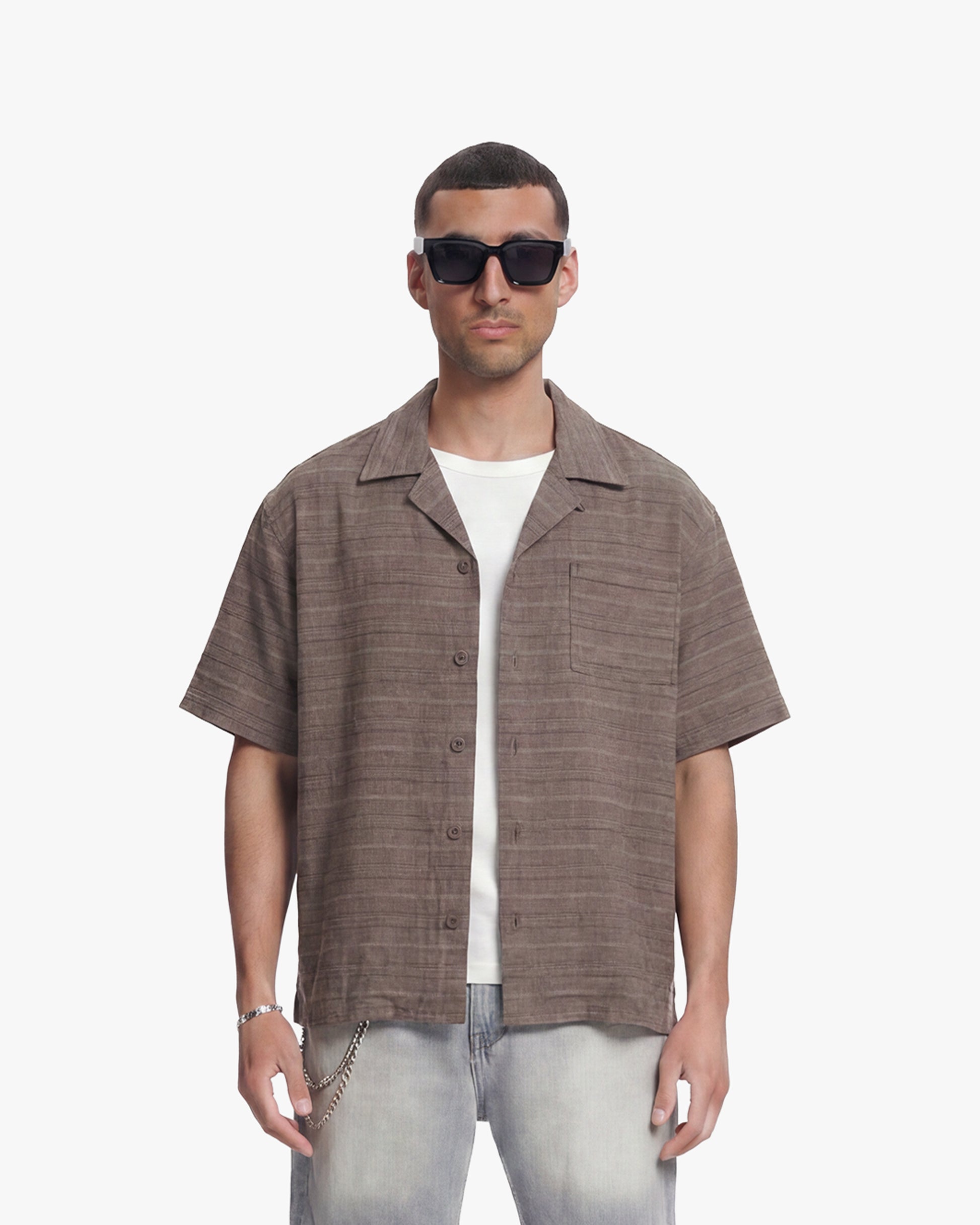 Man in vintage brown flannel shirt, short-sleeved with chest pocket, over a white tee and light wash jeans.