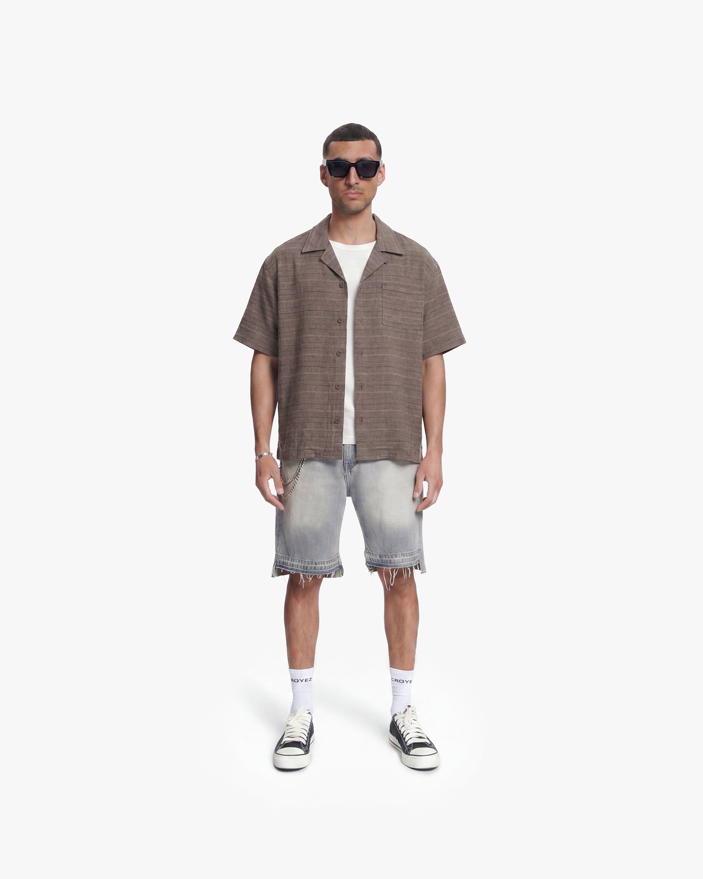 Man wearing a vintage washed brown flannel shirt, white tee, distressed denim shorts, and sunglasses.